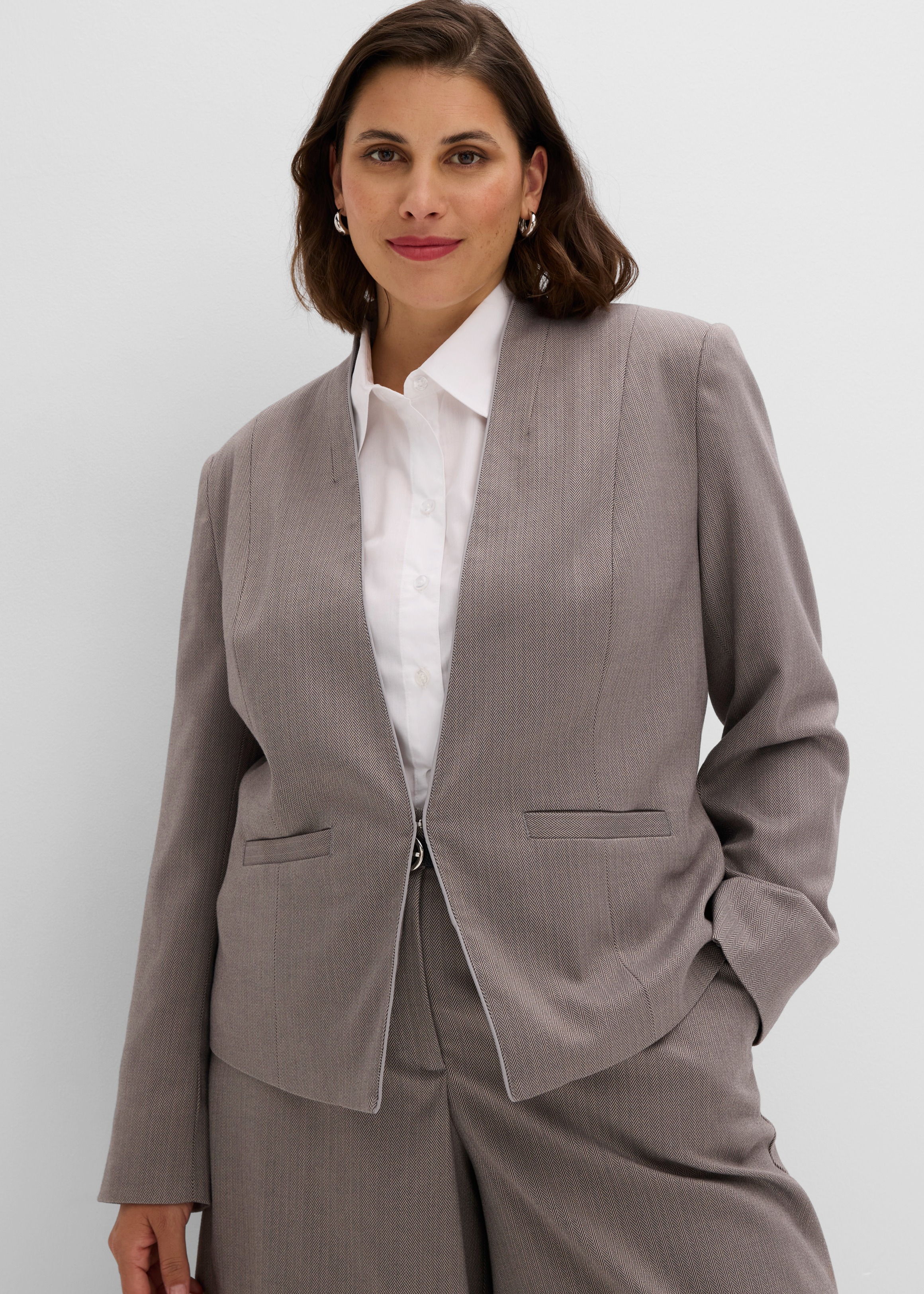 Die Frau trägt einen eleganten, gemusterten Blazer, eine weiße Bluse und Hose.