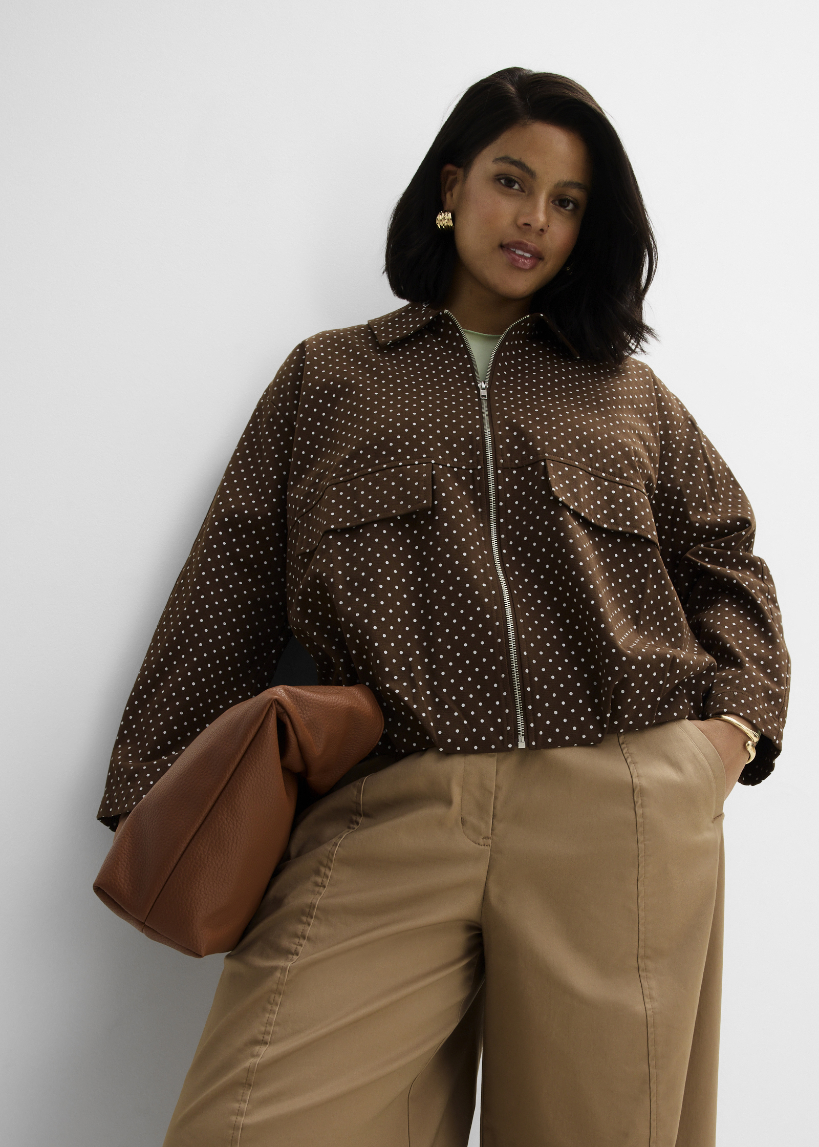 Modische braune Punkt-Jacke, weite beigefarbene Hose und elegante braune Clutch.