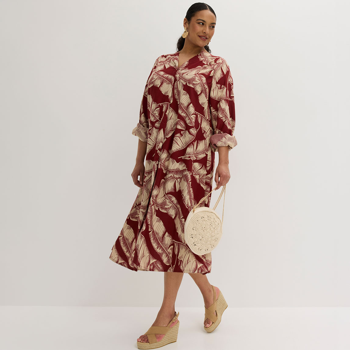 Rotes Midikleid mit tropischem Palmenmuster, kombiniert mit beigen Wedges und Basthandtasche.