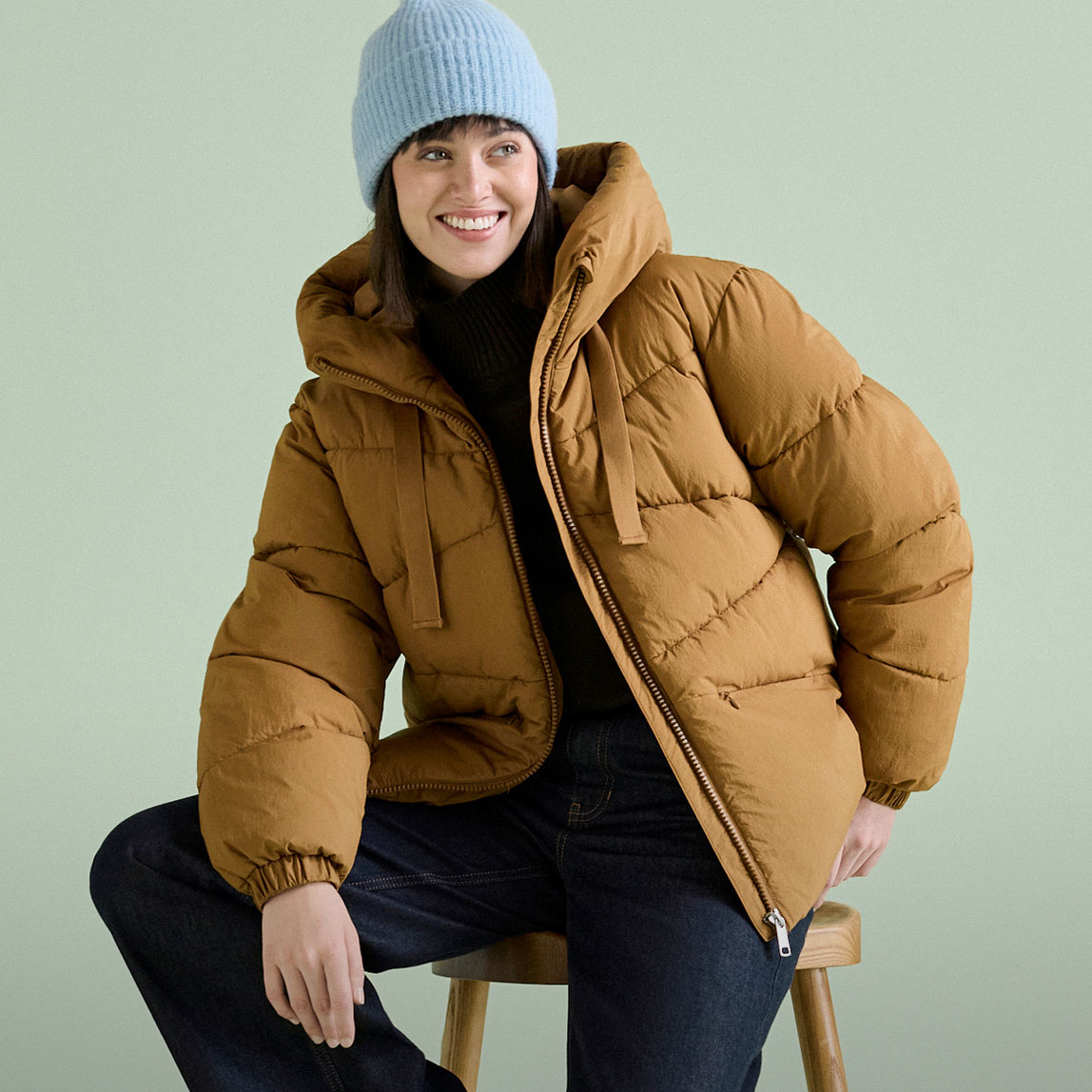 Blaue Mütze, braune Steppjacke und dunkle Jeans.
