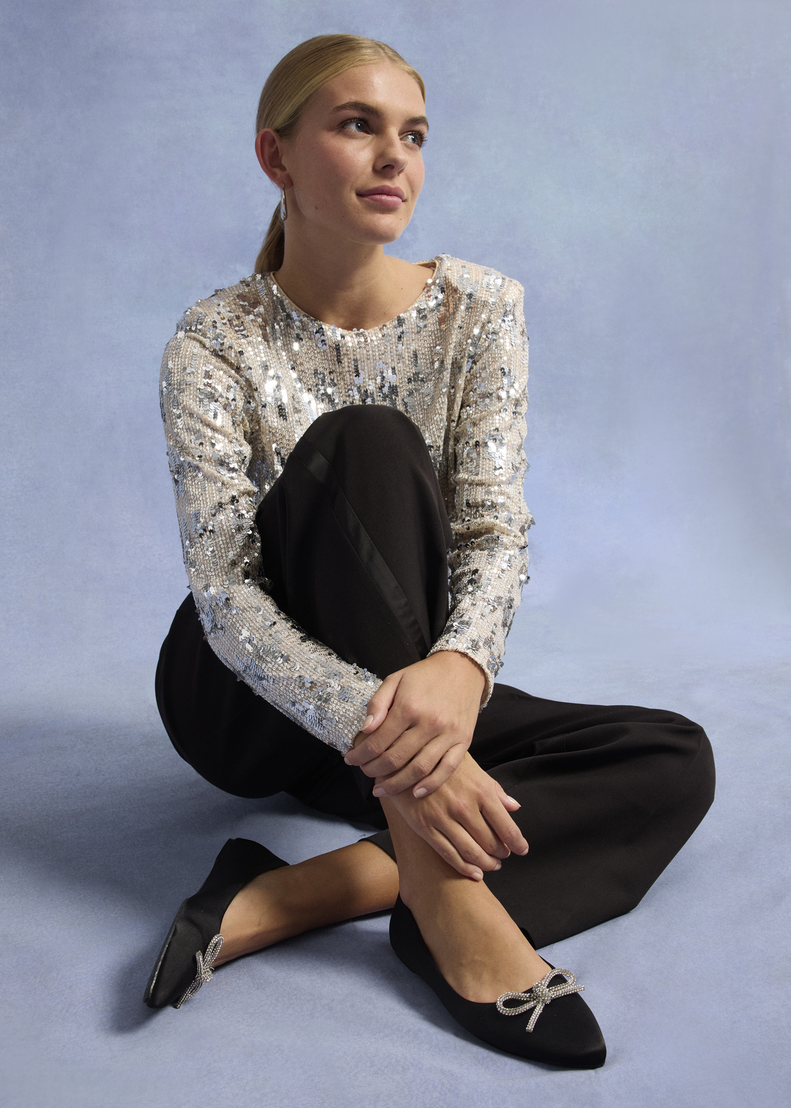 Glitzernde Pailletten-Bluse trifft auf schlichte schwarze Hose und spitze Ballerinas.