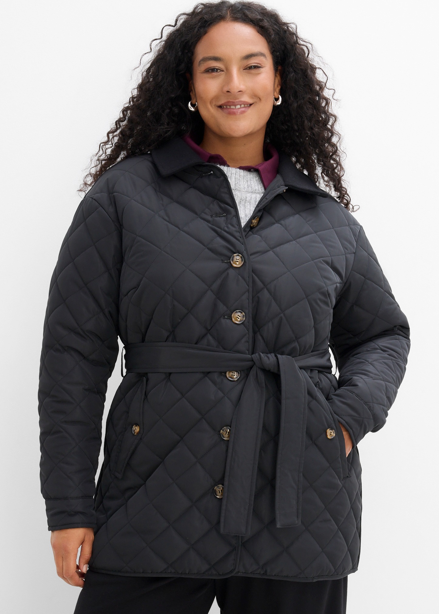 Elegante schwarze Steppjacke mit Gürtel, kombiniert mit Pullover und Hemdkragen.