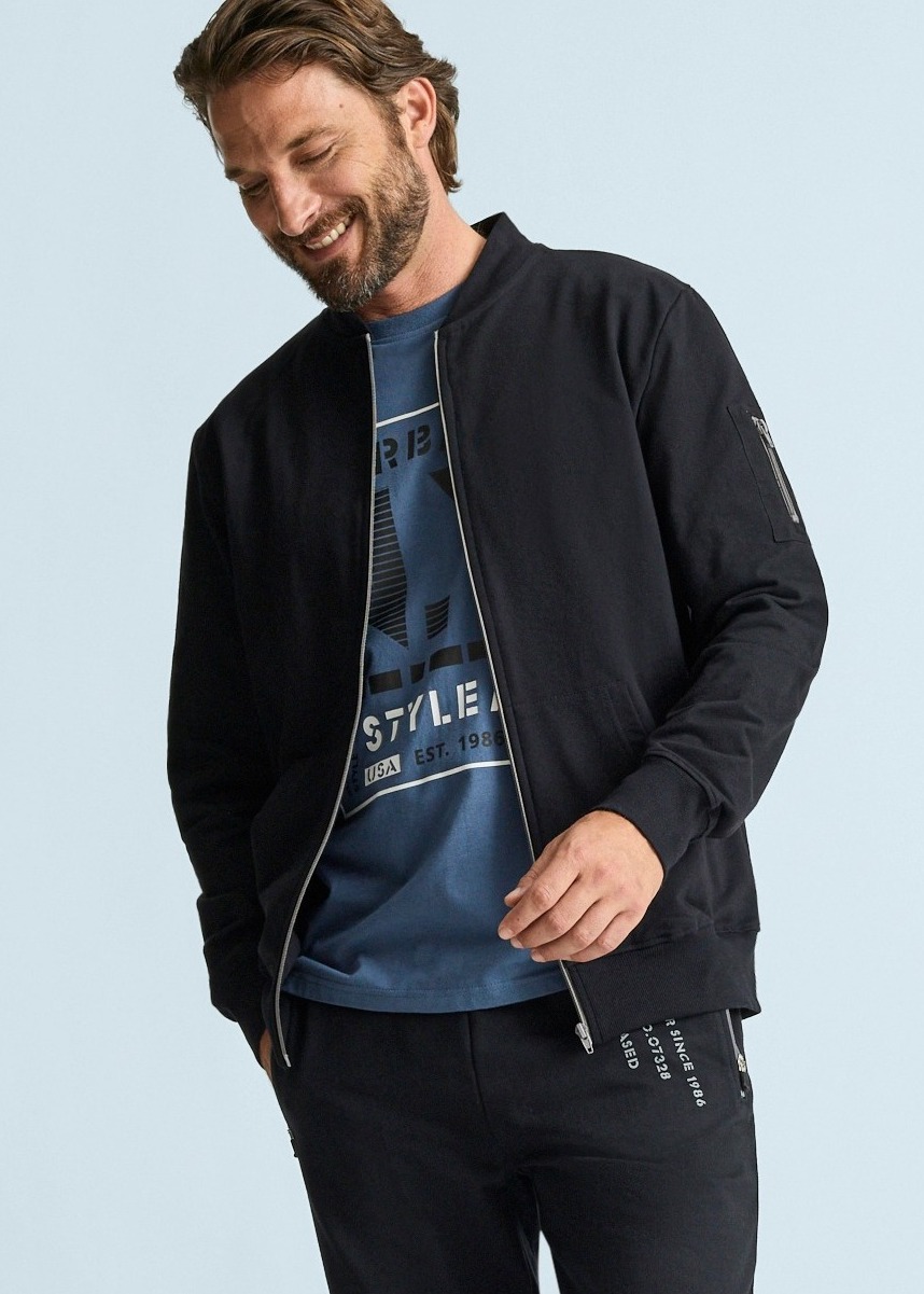  Schwarze Bomberjacke, blaues Print-Shirt und passende schwarze Hose.