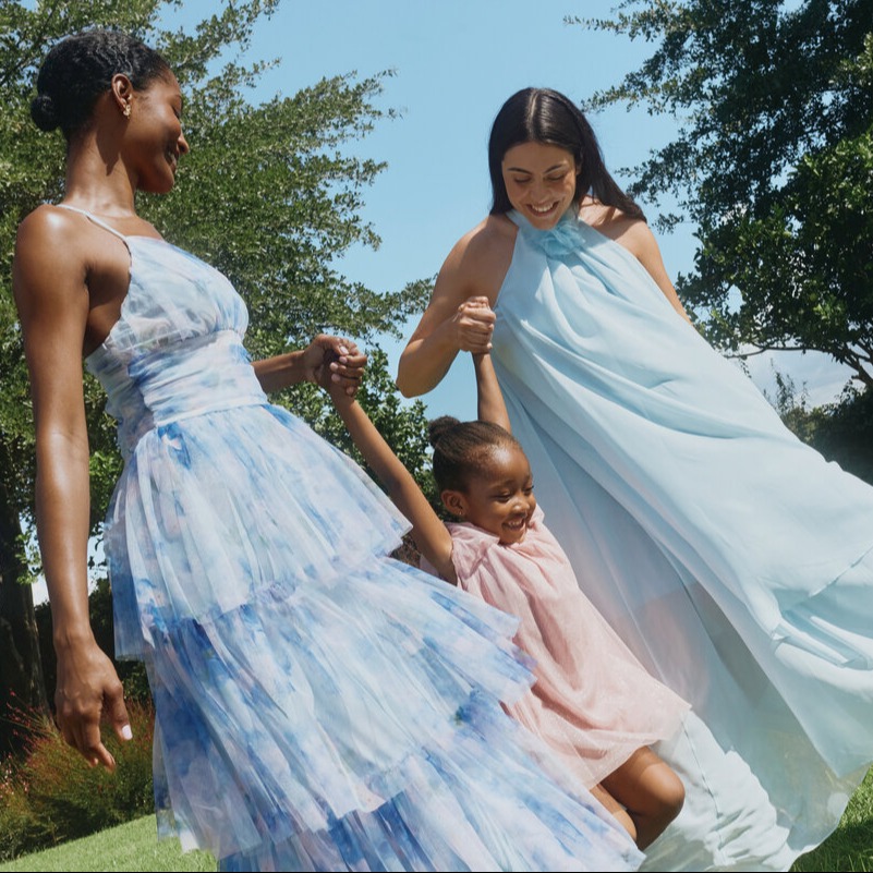 Zwei Frauen und ein Kind tragen elegante, luftige Sommerkleider in Pastelltönen.