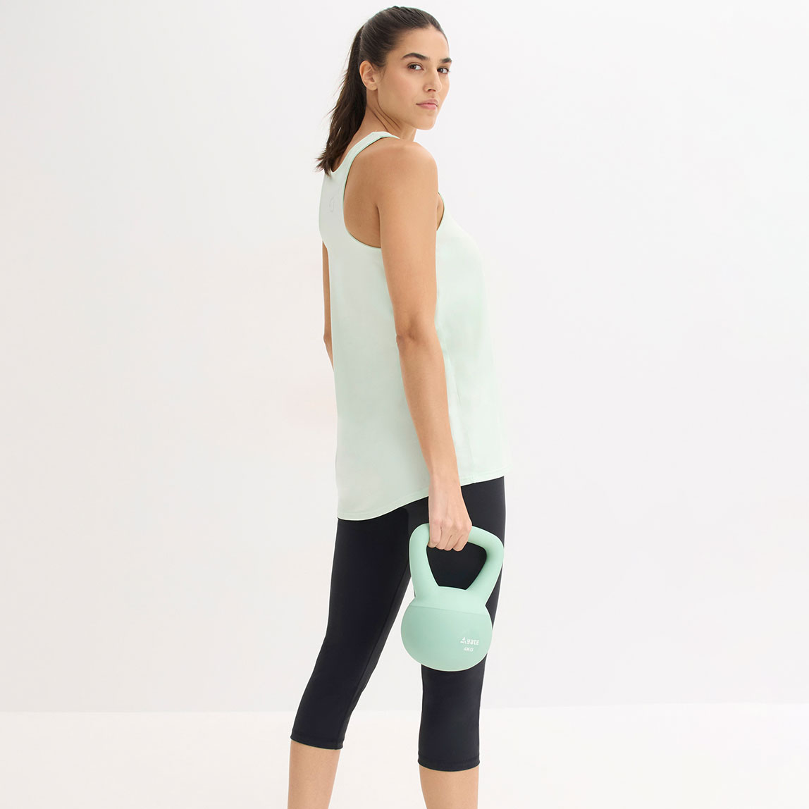 Sportliche Frau trägt mintgrünes Top und schwarze Leggings für das Workout.