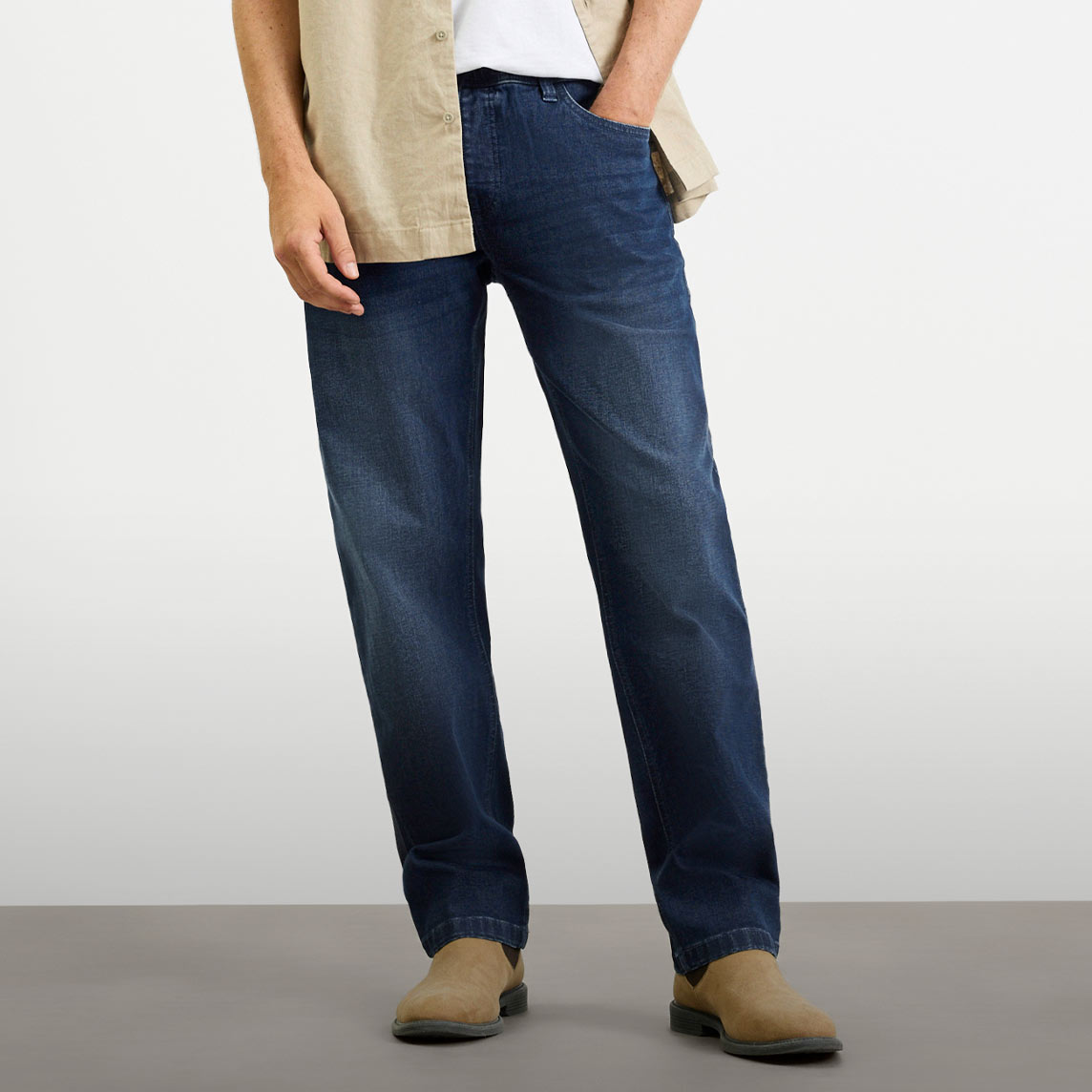 Dunkelblaue Jeans, helles Hemd, weißes T-Shirt und braune Schuhe für lässigen Stil.