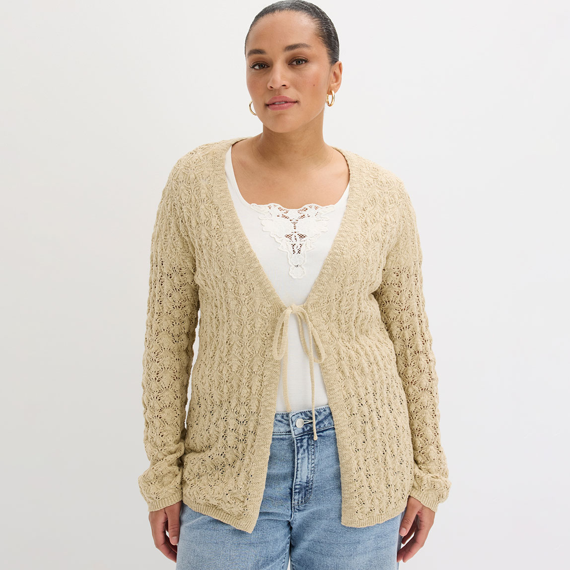 Beige Strickjacke über weißem Top kombiniert mit klassischer blauer Jeans.