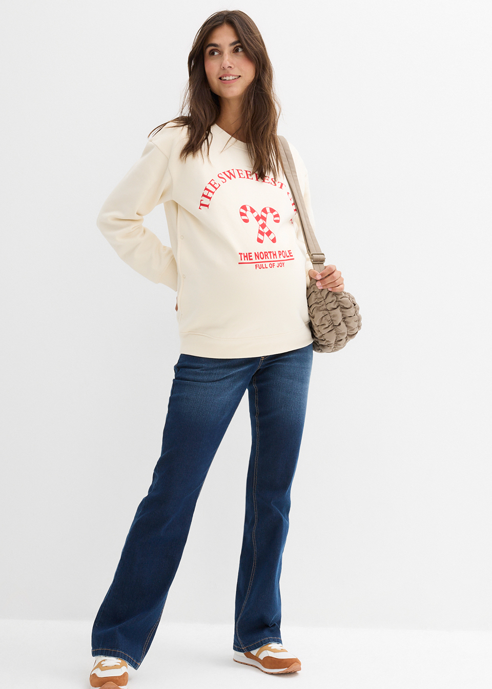 Frau trägt beigen Pullover mit rotem Aufdruck, dunkle Jeans und braune Tasche.