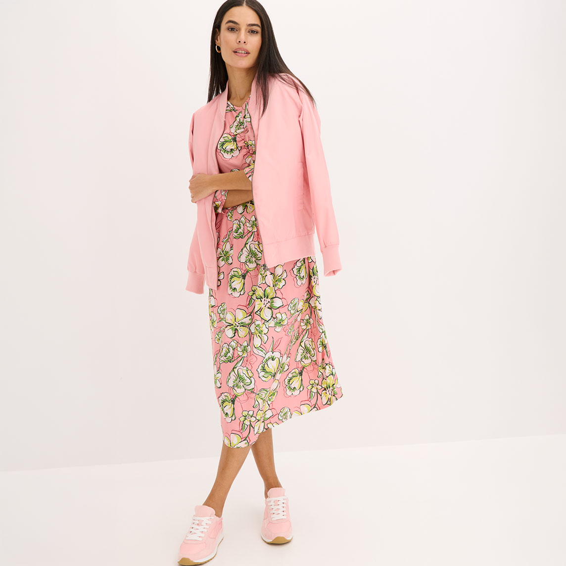 Frau trägt rosa Blouson über buntem Blumenkleid mit passenden rosa Schuhen.