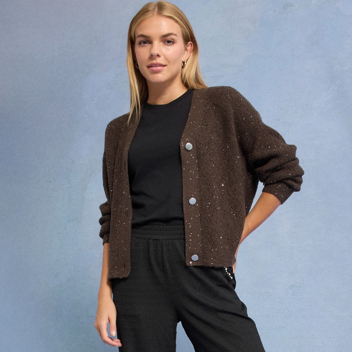 Glitzernde braune Strickjacke über schwarzem Outfit.