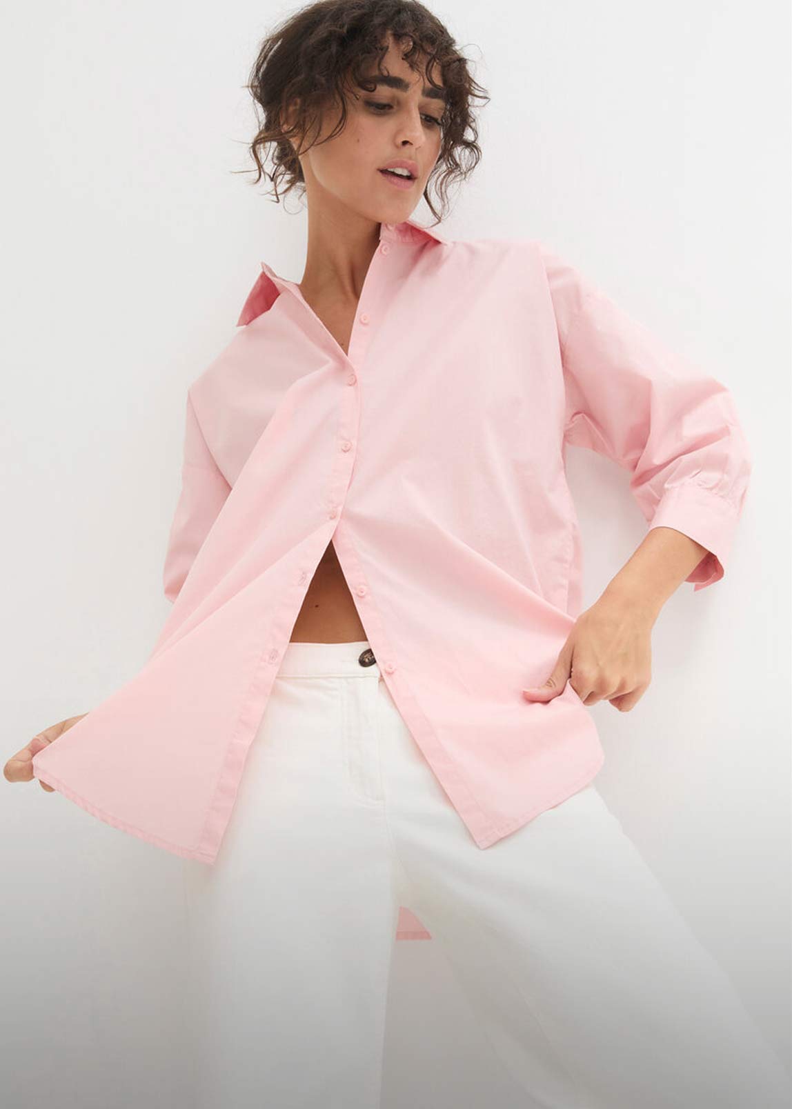 Zartrosa Hemdbluse mit langen Ärmeln über weißer Hose.