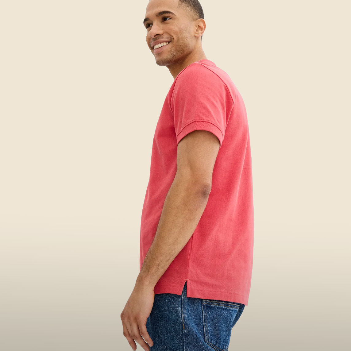 Er trägt ein leuchtend rotes Poloshirt und bequeme blaue Jeans.