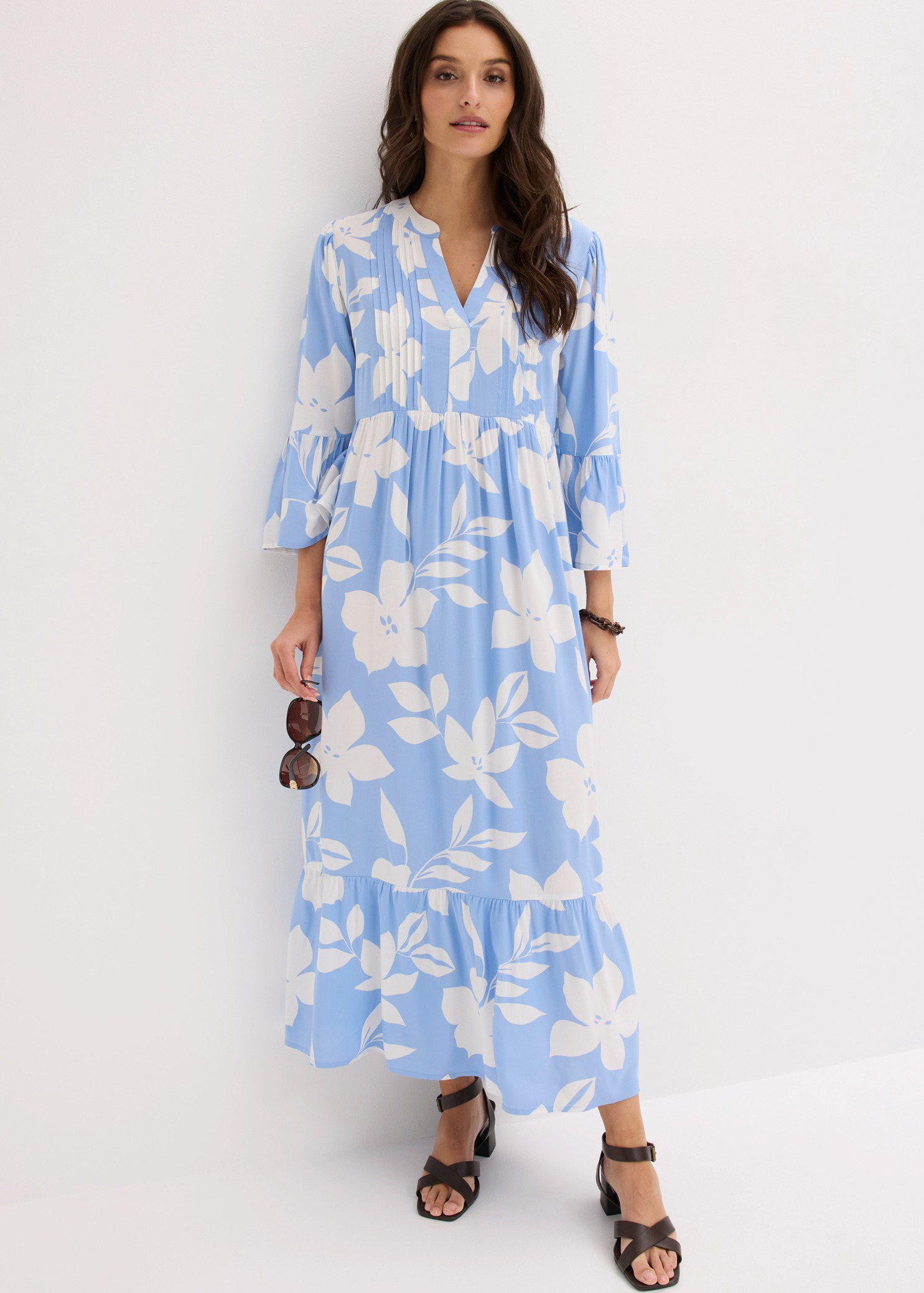 Ein langes, hellblaues Kleid mit weißem Blumenmuster, V-Ausschnitt und braunen Sandalen.