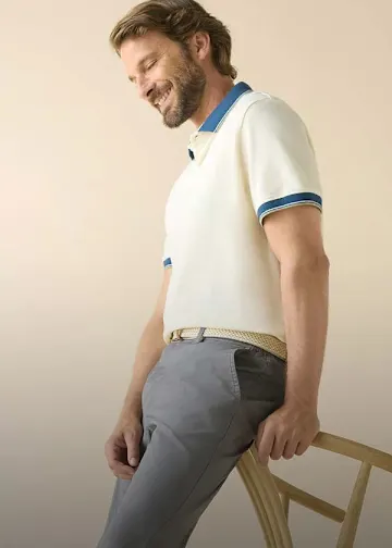 Beiges Poloshirt mit blauen Details, graue Hose und geflochtener Gürtel.