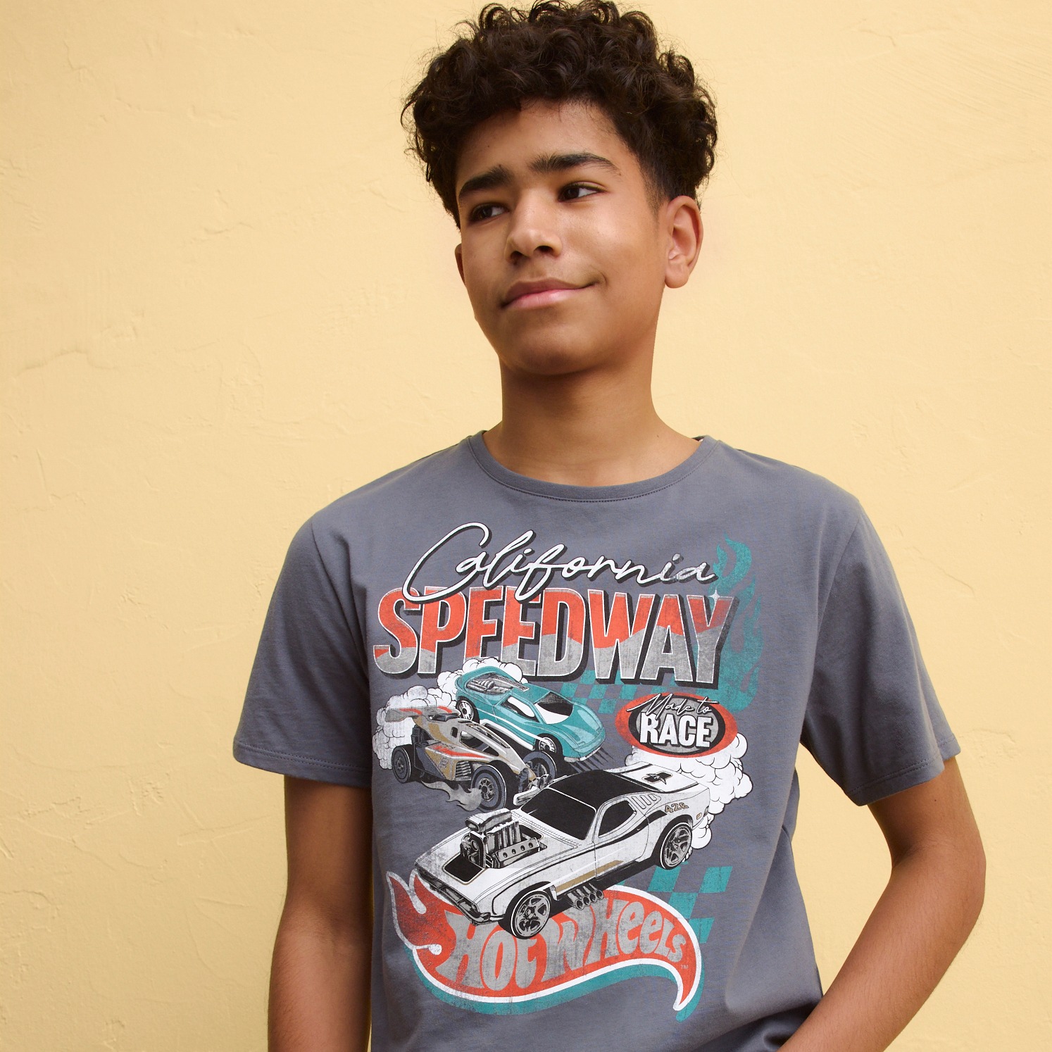 Junge trägt graues T-Shirt mit buntem California Speedway Rennwagen-Aufdruck.