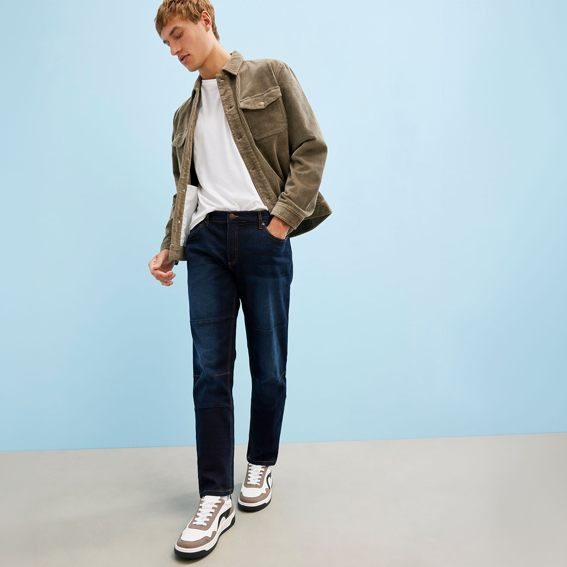 Lässige Kombination aus weißem Shirt, Cordjacke, Jeans und modernen Sneakern.