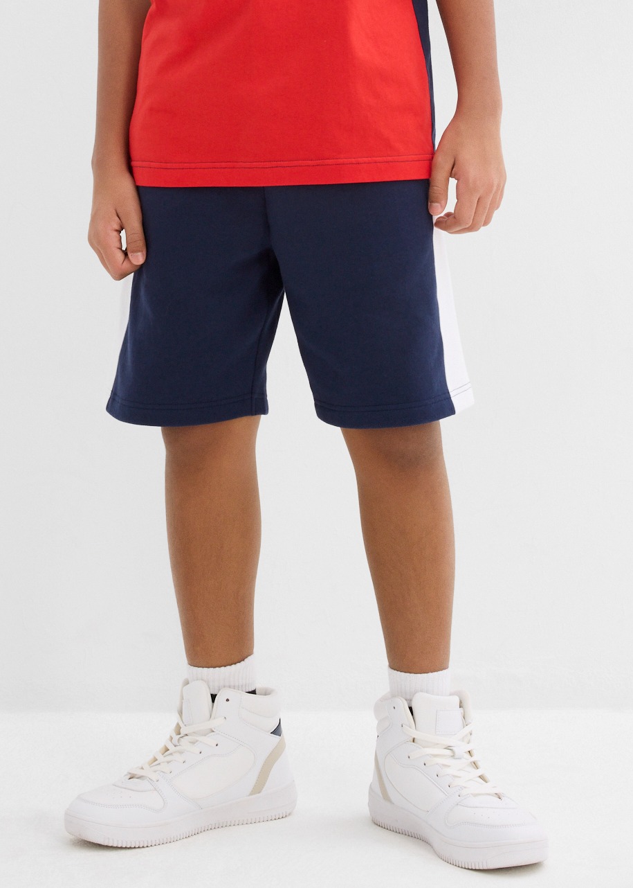 Ein Kind trägt ein rotes Oberteil, dunkelblaue Shorts.