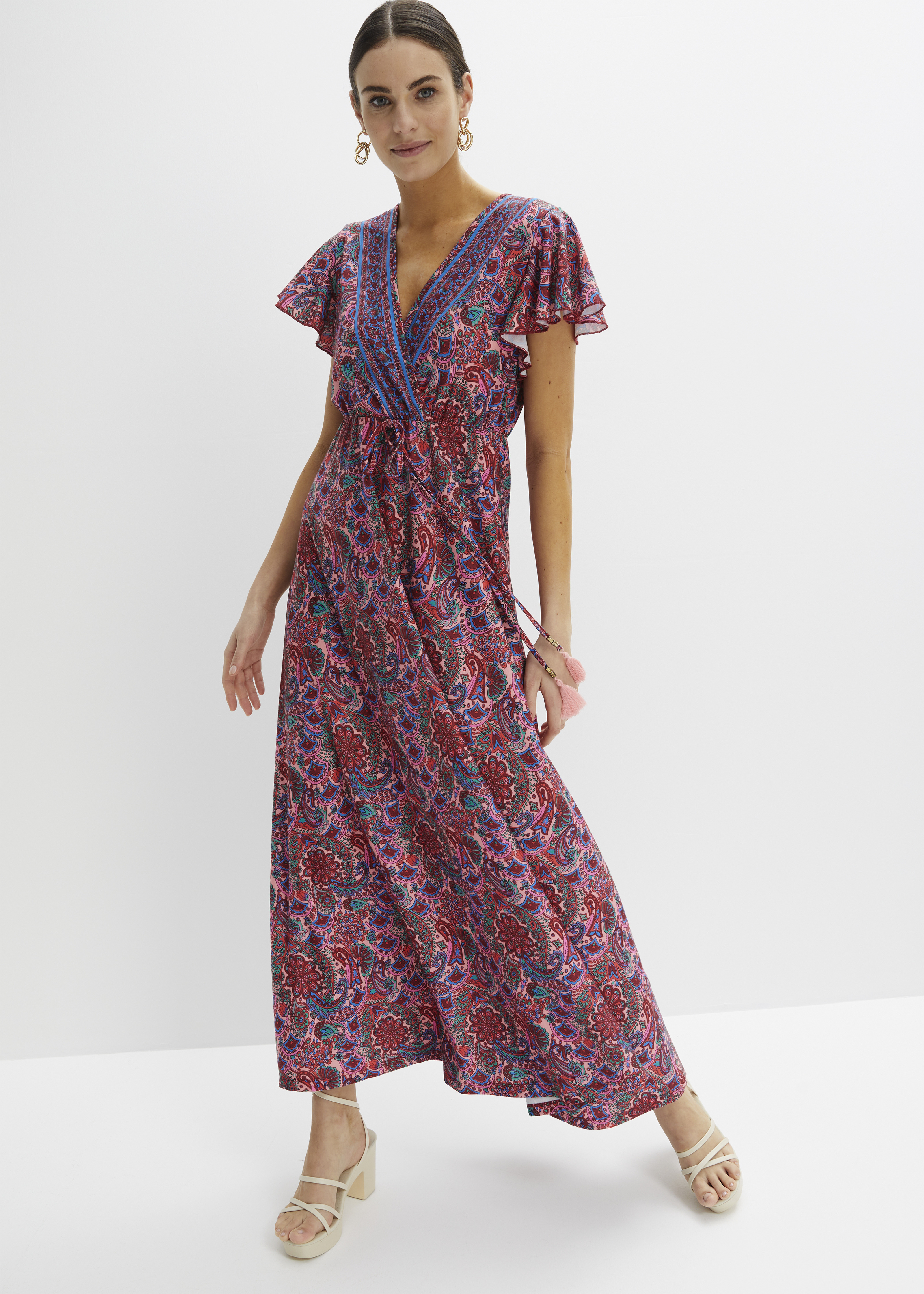 Lebhaft gemustertes Maxikleid mit V-Ausschnitt, flatternden Ärmeln und hellen Plateausandalen.