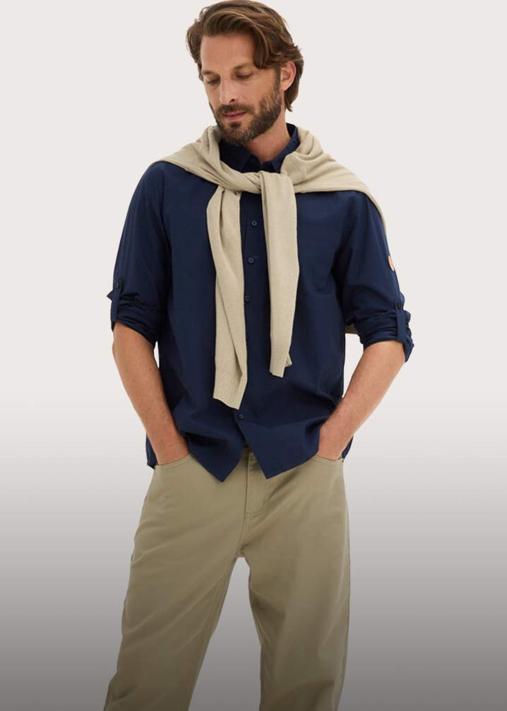 Dunkelblaues Hemd mit hochgekrempelten Ärmeln, beige Hose und heller Pullover.