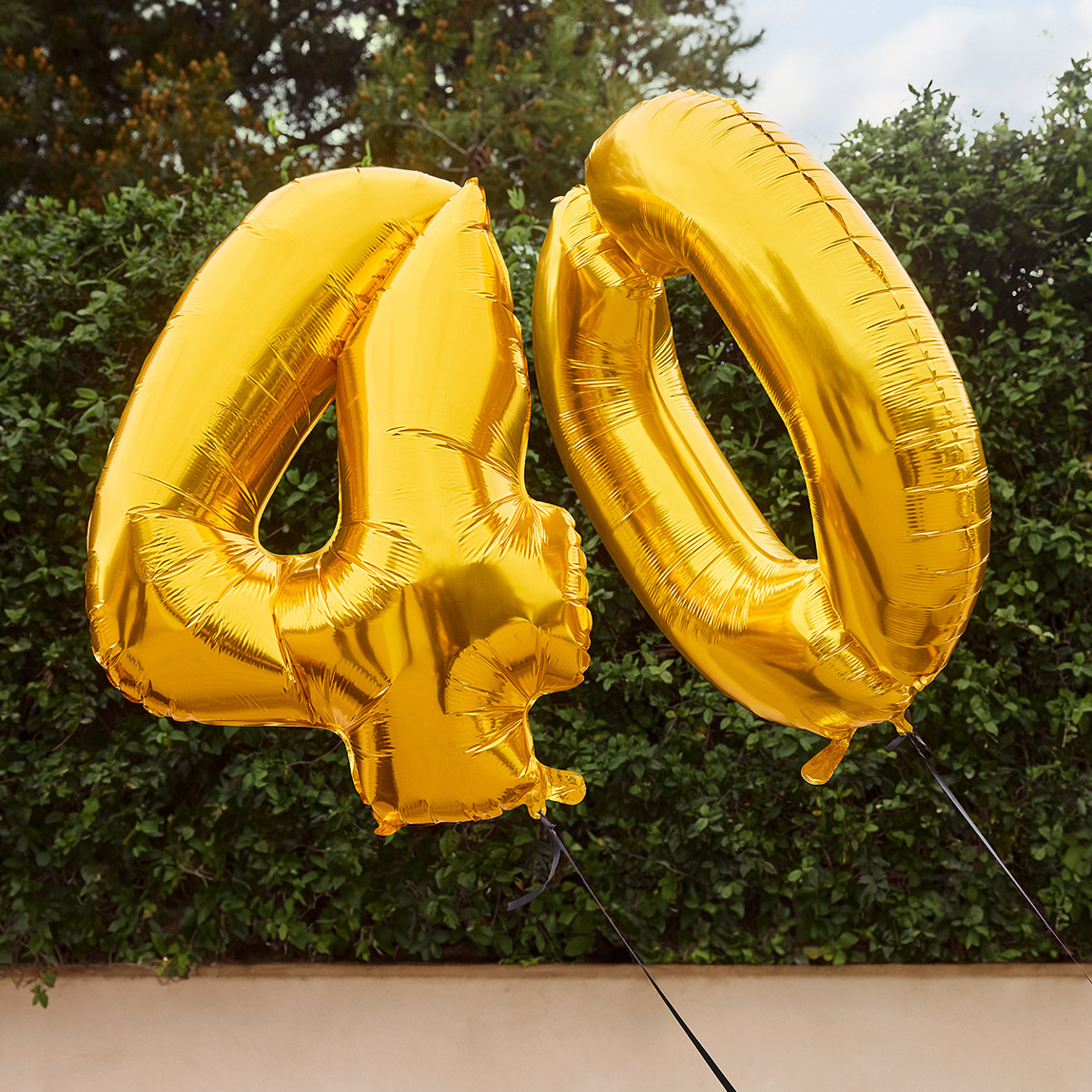 Goldene Luftballons in Form der Zahl 40 schweben im Freien vor grünem Hintergrund.