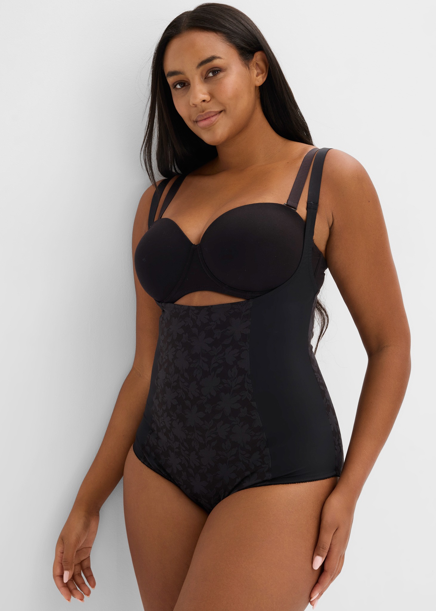 Eine Frau präsentiert stilvolle schwarze Shapewear mit einem trägerlosen BH und Musterdetail.