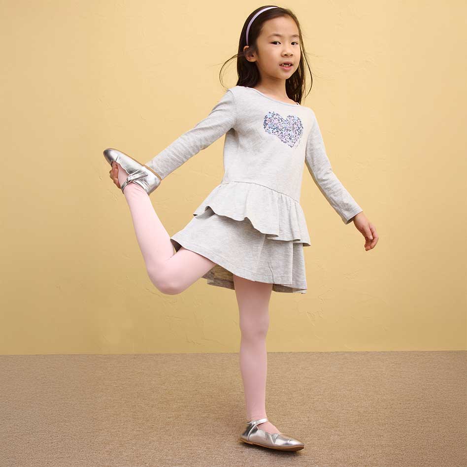 Ein Mädchen trägt ein graues Kleid mit Rüschen und rosa Leggings.
