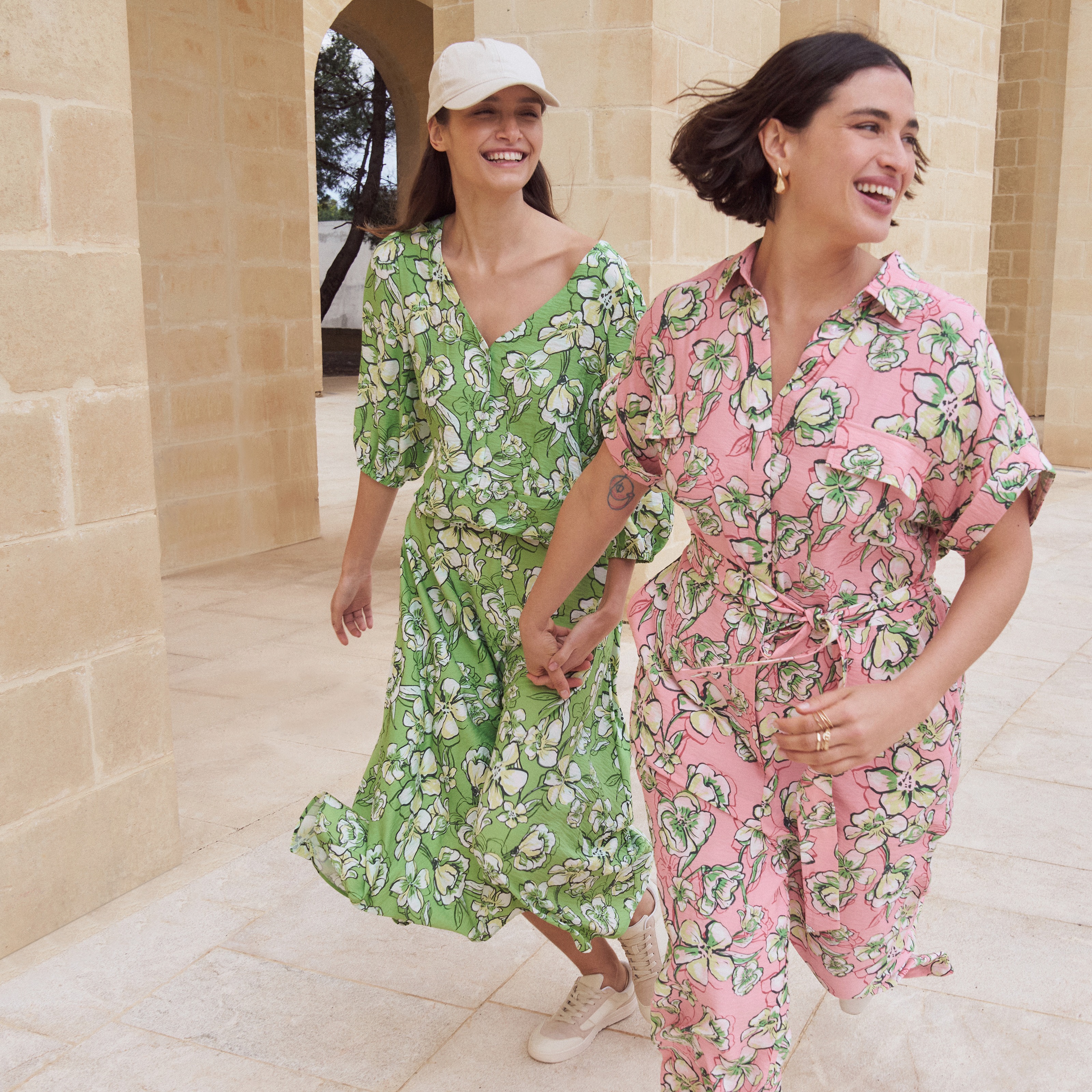 Sommerliche Kleider mit floralem Muster in Grün und Rosa, dazu eine weiße Kappe.