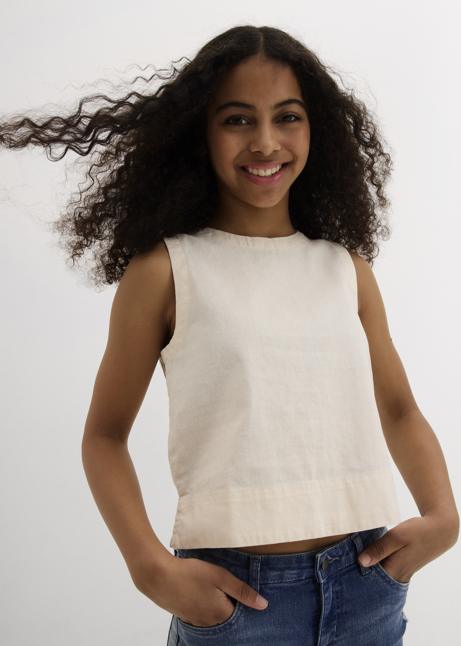 Hellbeiges ärmelloses Top und blaue Jeans.
