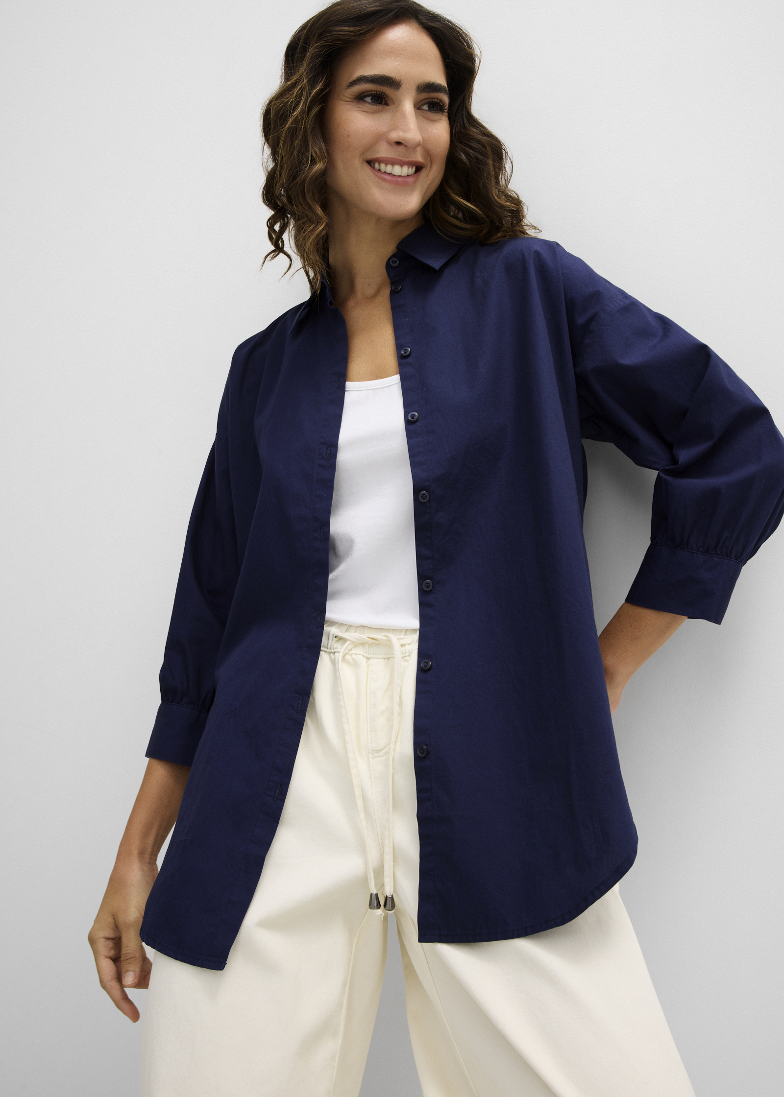 Die Frau trägt ein marineblaues Oversize-Hemd über einem weißen Top und helle Hose.