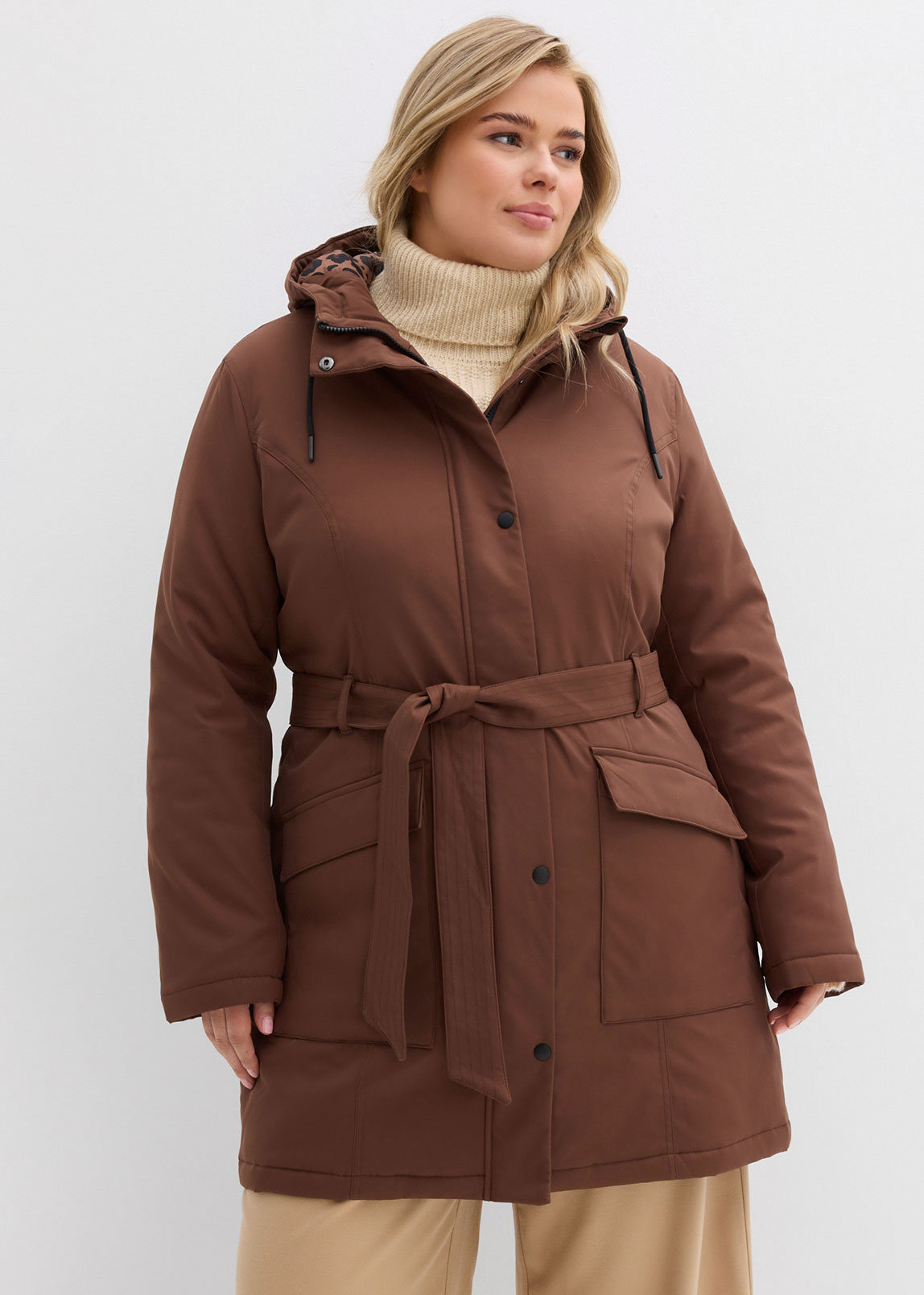 Brauner Mantel mit Gürtel, kombiniert mit beigem Rollkragenpullover und heller Hose.