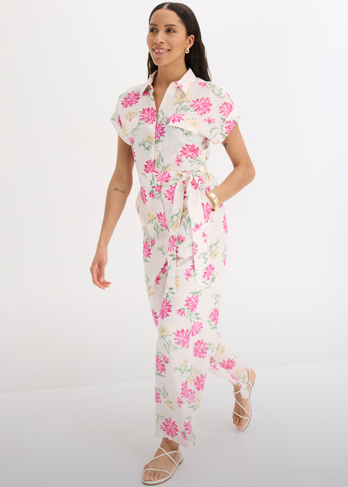 Eleganter weißer Overall mit pinkem Blumenmuster, kurzen Ärmeln und passenden Sandalen.