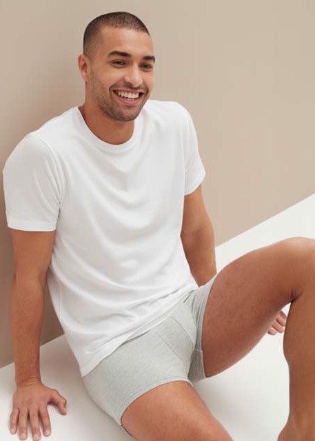 Ein Mann in einem schlichten weißen T-Shirt und hellgrauen Boxershorts.