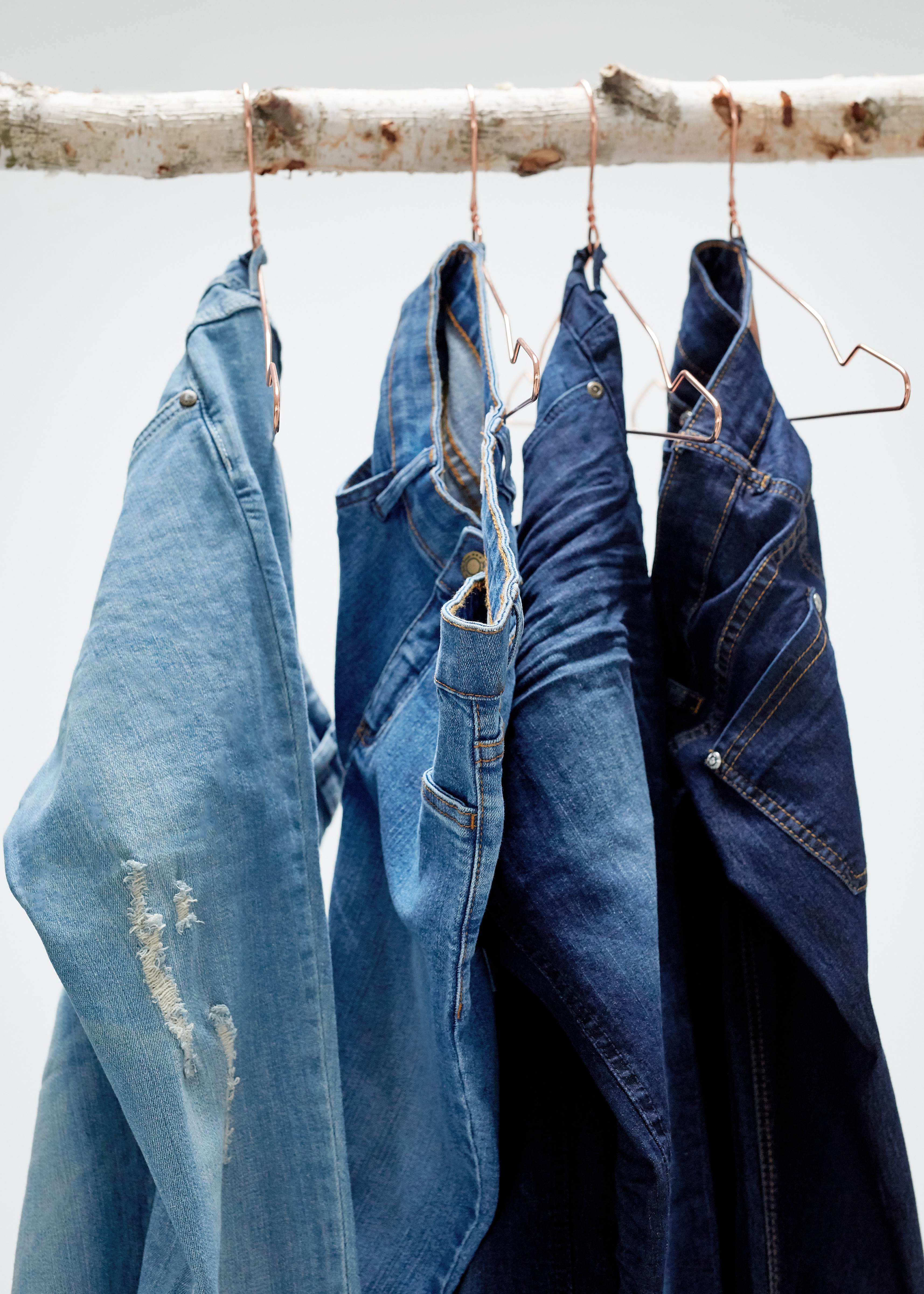 Jeans in verschiedenen Blautönen hängen an Bügeln auf einem Holzast.