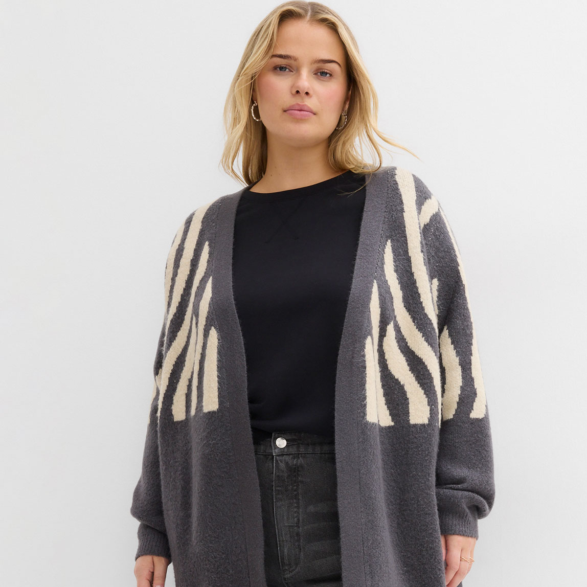 Grauer Cardigan mit Zebramuster, schwarzes Oberteil und Jeans. 