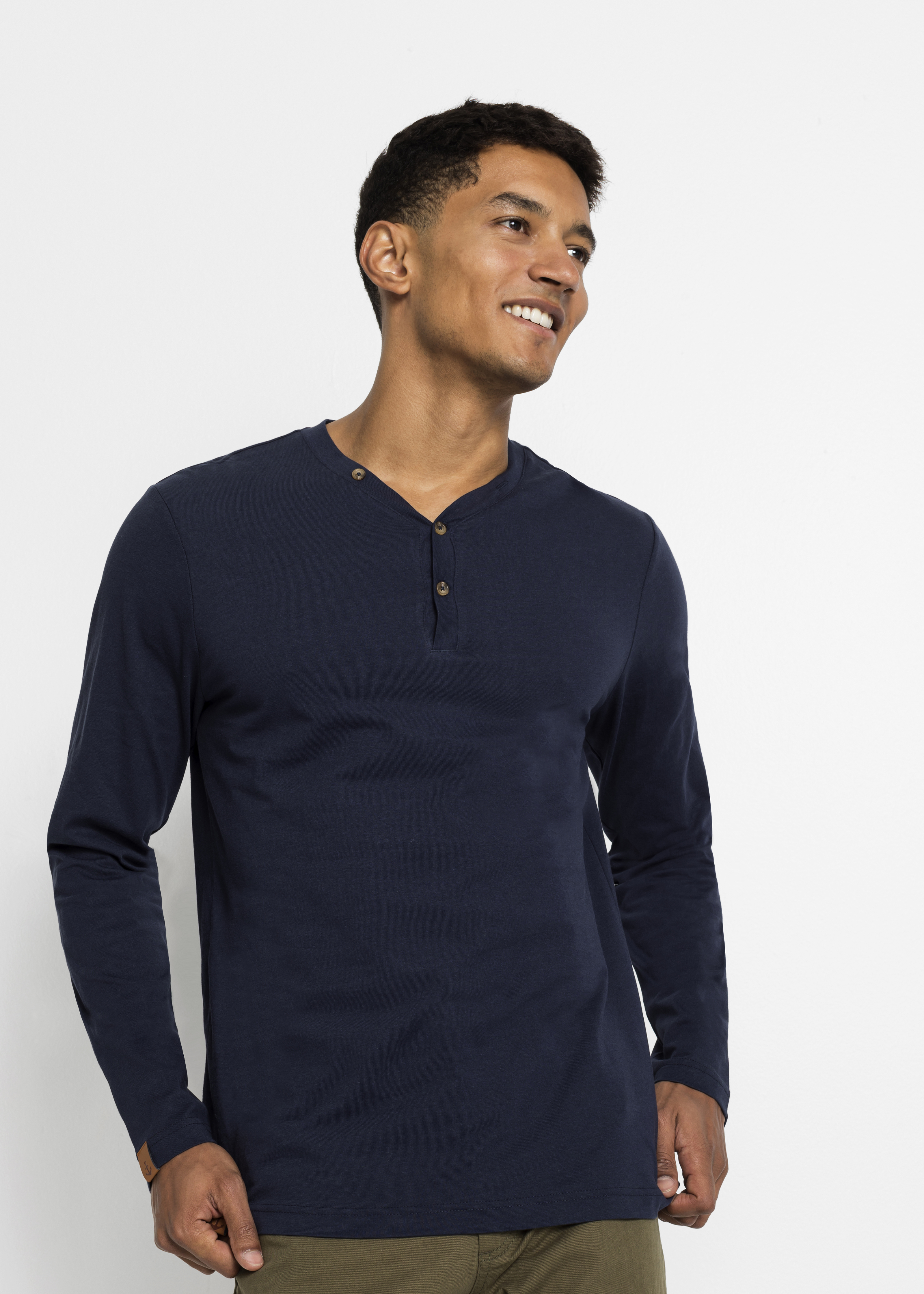 Ein Mann trägt ein dunkelblaues Langarmshirt mit Knopfleiste und eine olivgrüne Hose.