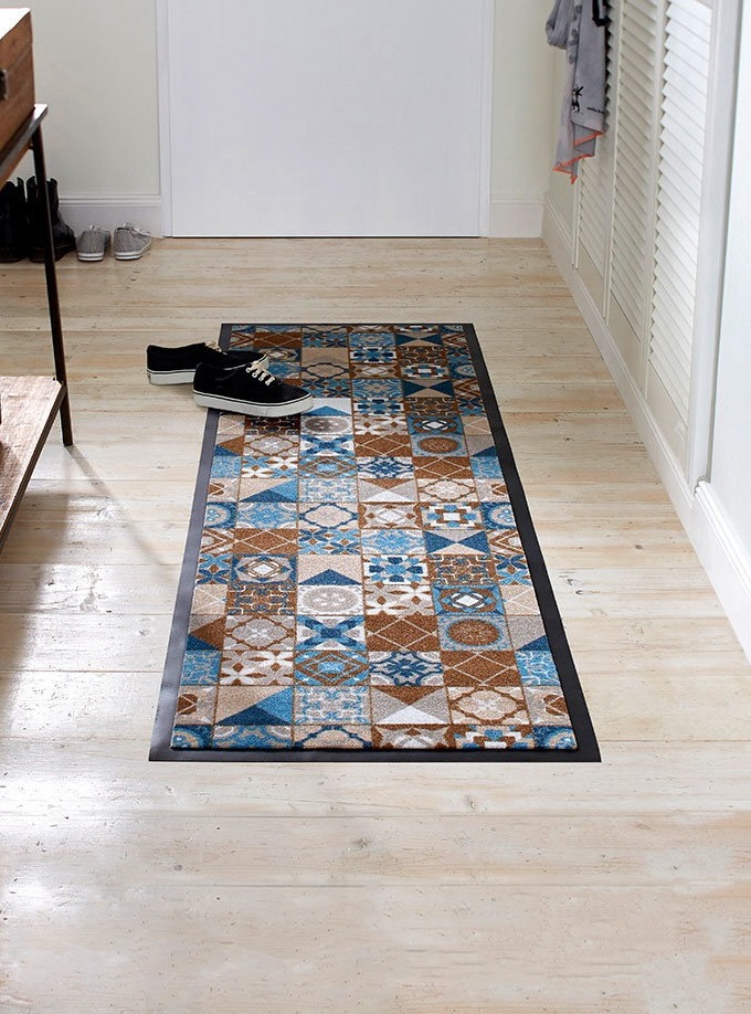 Schwarze Schuhe ruhen auf buntem Teppich mit geometrischem Muster im hellen Raum.