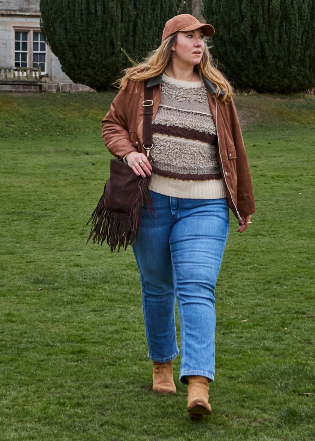  Braune Jacke, gemustertem Pullover, Jeans und Cap.