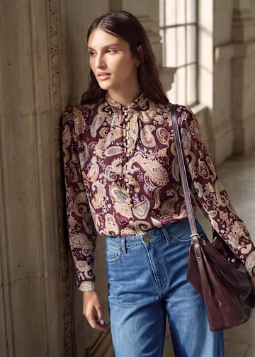 Modischer Look: Paisley-Bluse, weite Jeans, schicke Schuhe und passende Handtasche.