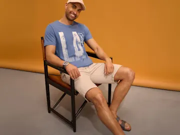 Lässiger Look: Kappe, blaues T-Shirt mit Print, beige Shorts und Armbanduhr.