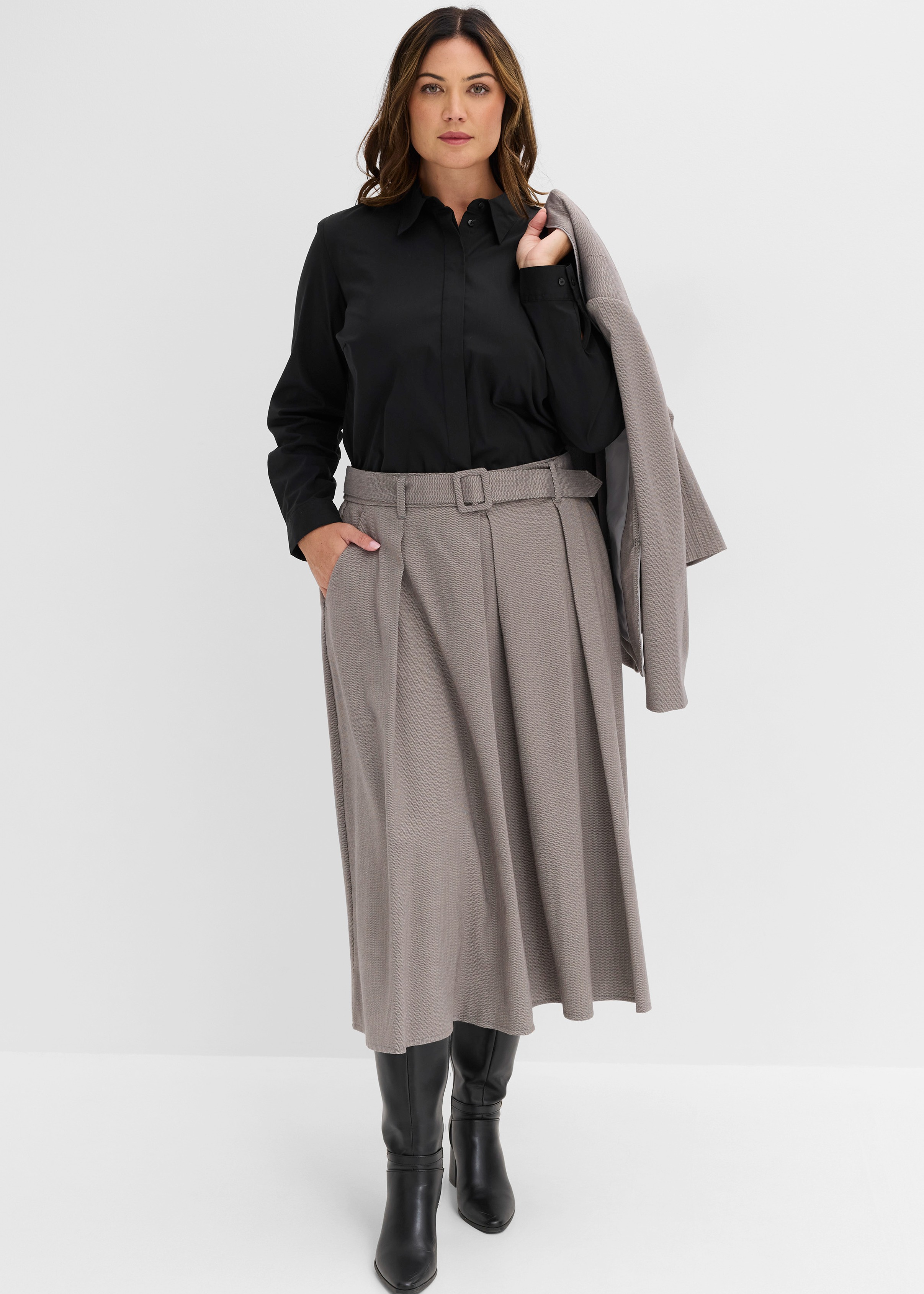 Elegante schwarze Bluse, beiger Faltenrock mit Gürtel, Stiefel und ein passender Blazer.