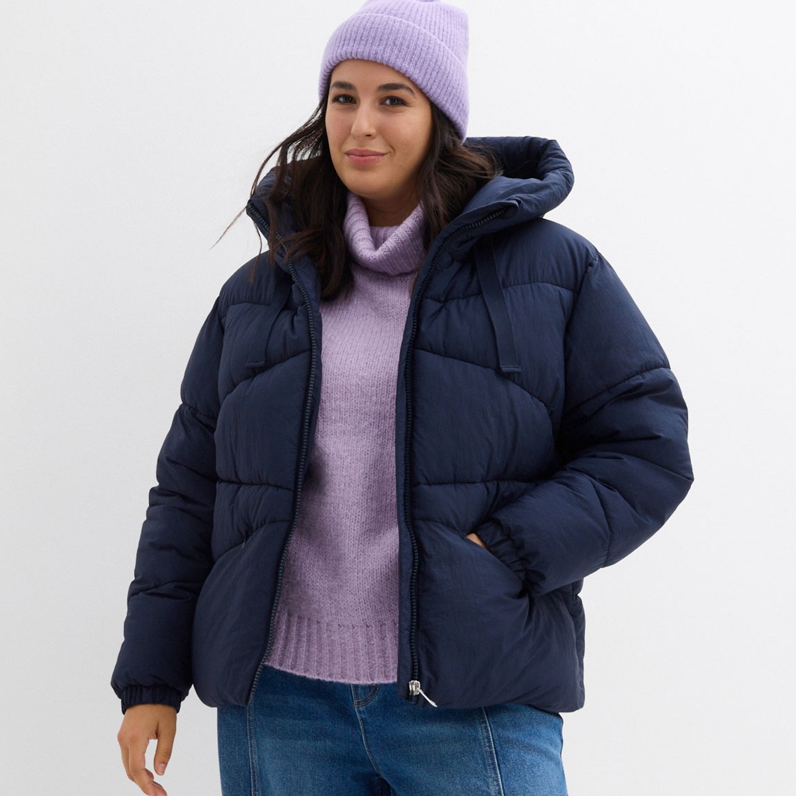 Dunkelblaue Daunenjacke, lila Rollkragen und Strickmütze.