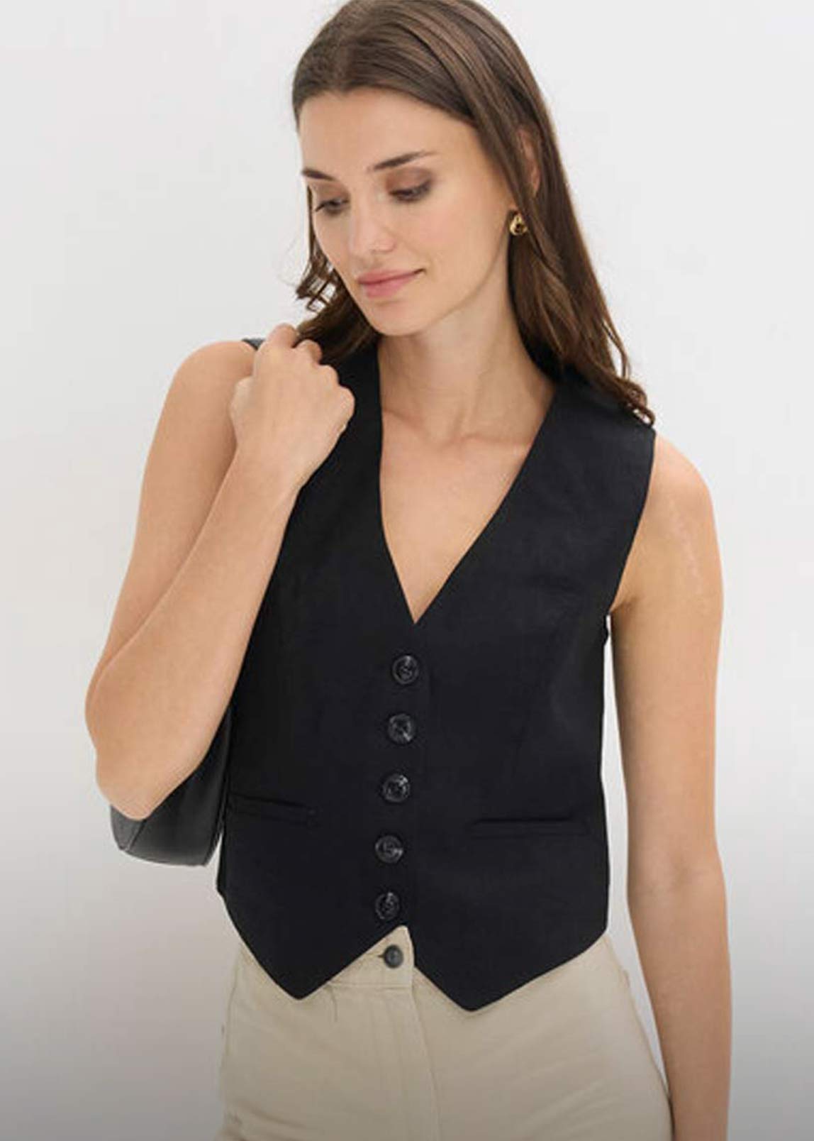 Elegante schwarze Weste über weißem Top, kombiniert mit heller Hose.