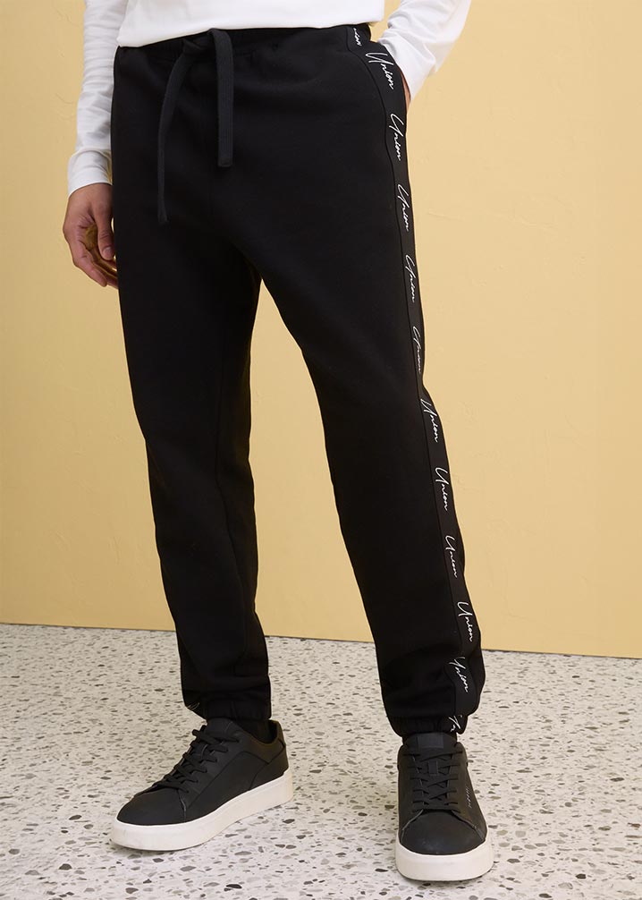 Schwarze Jogginghose mit weißem Schriftzug an der Seite.