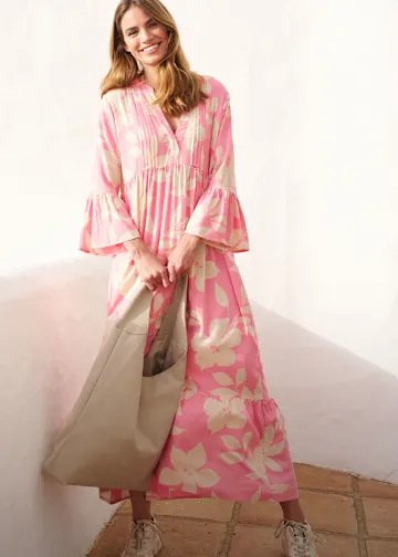 Sie trägt ein fließendes rosa Blumenkleid, eine große beige Tasche und Sneaker.