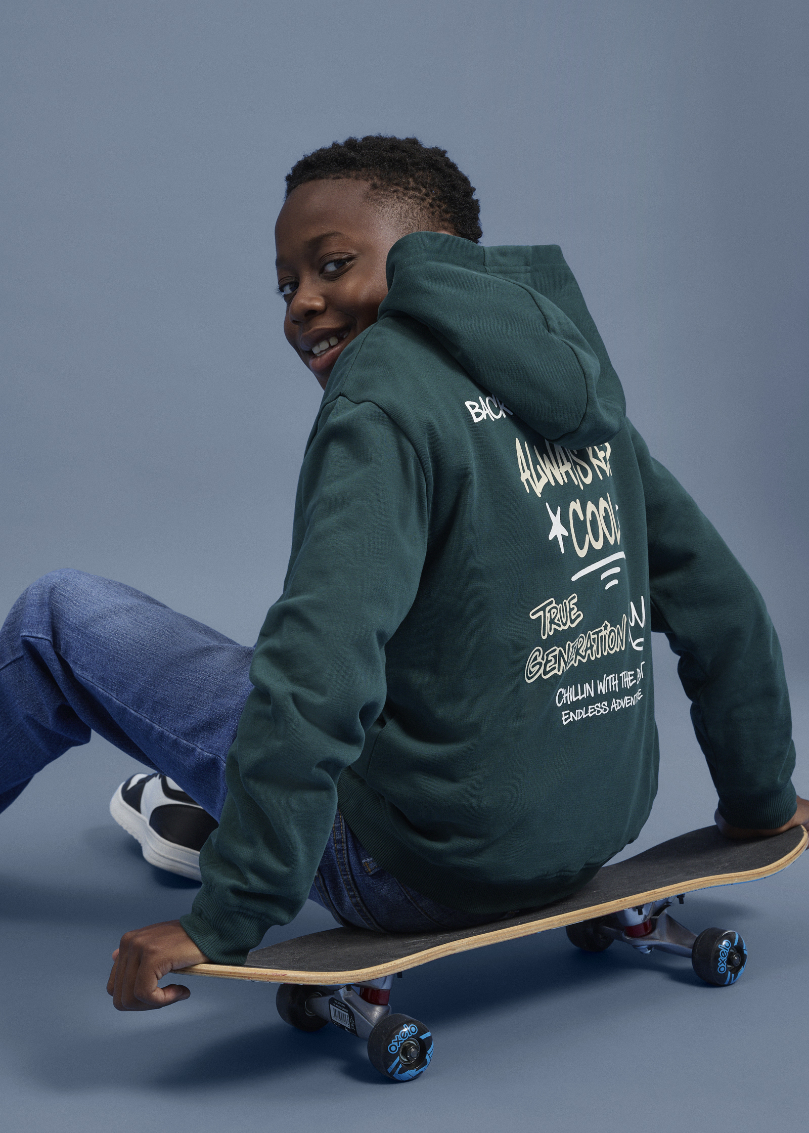 Grüner Hoodie mit Aufdruck, blaue Jeans und Sneakers für einen coolen Skater-Look.