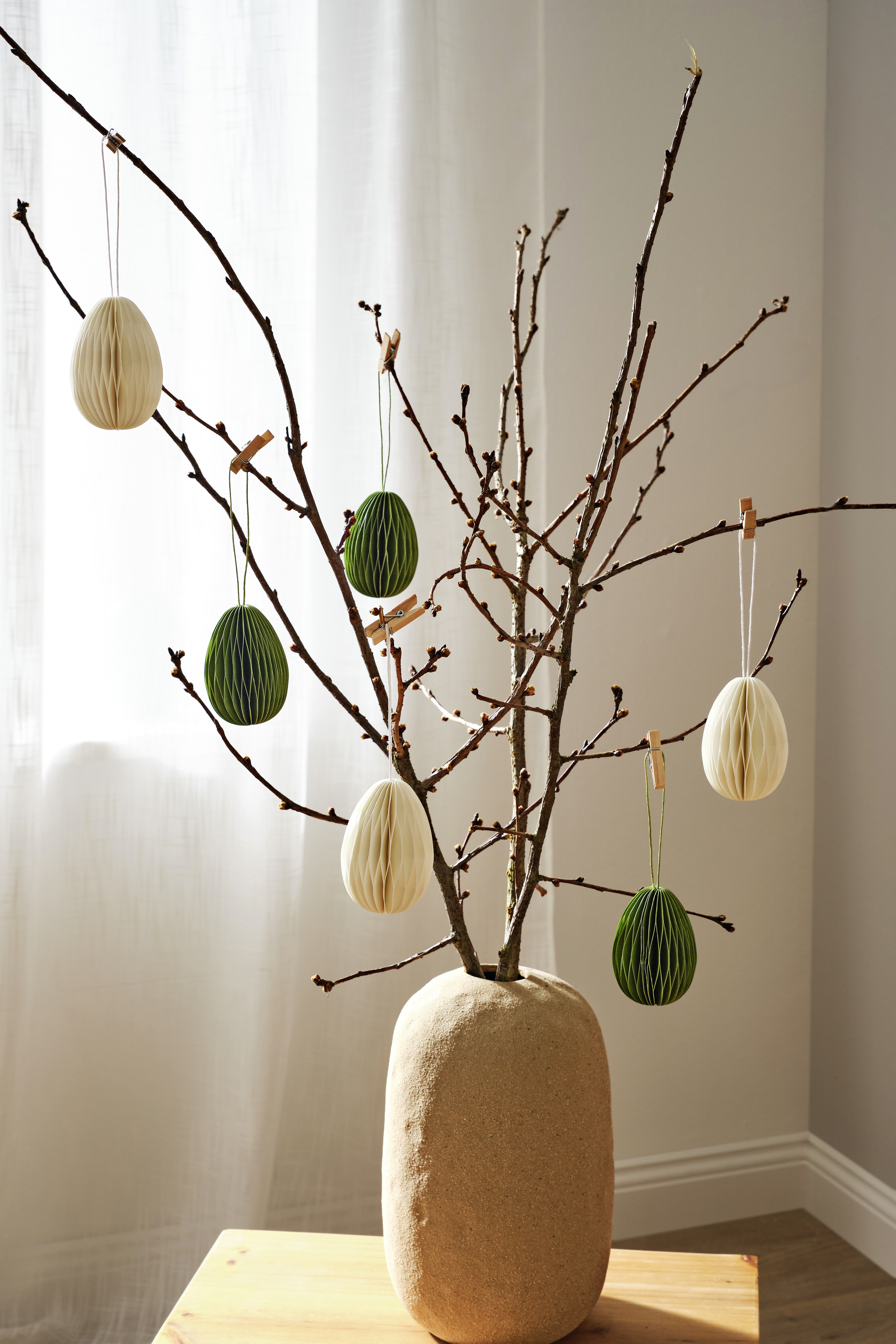 Oster Dekoration mit Zweigen und Papiereiern in Weiß und Grün.