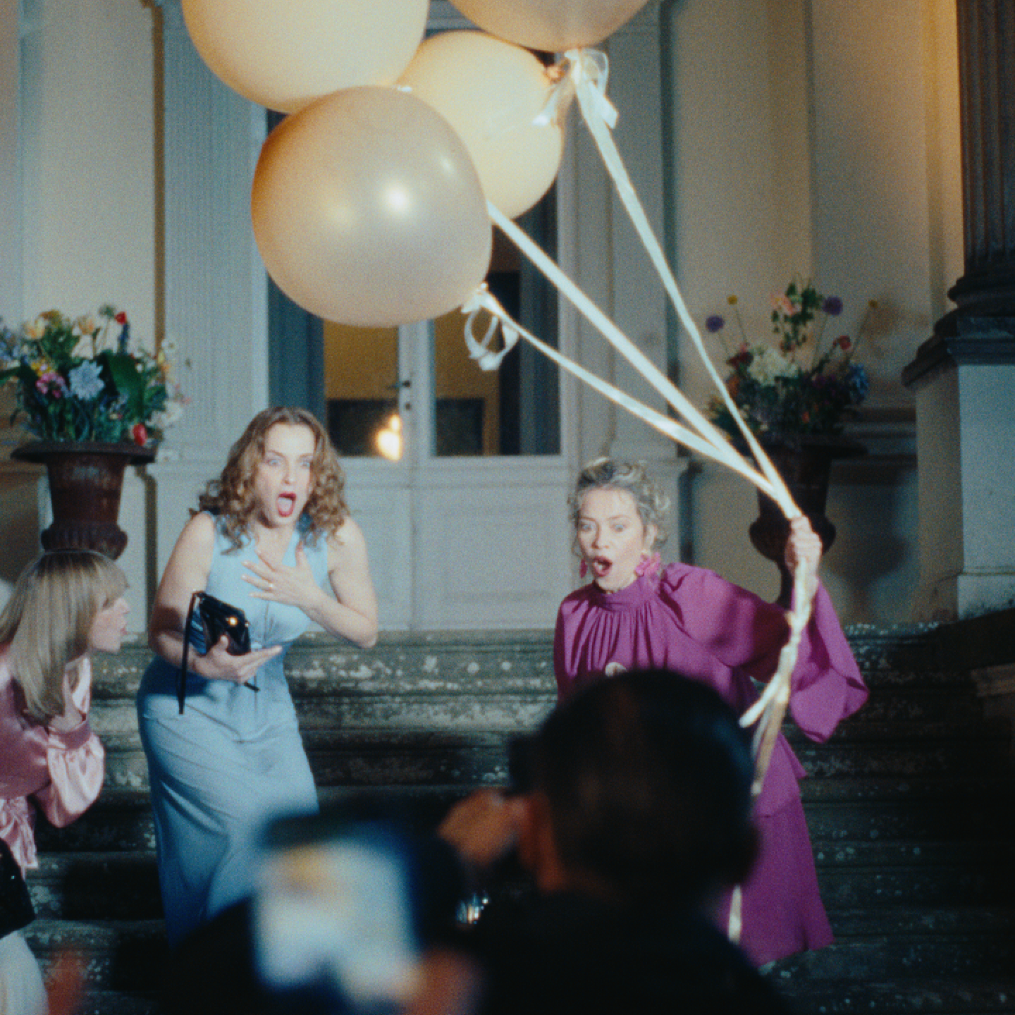 Zwei Frauen schauen überrascht und die eine hält Luftballons fest.