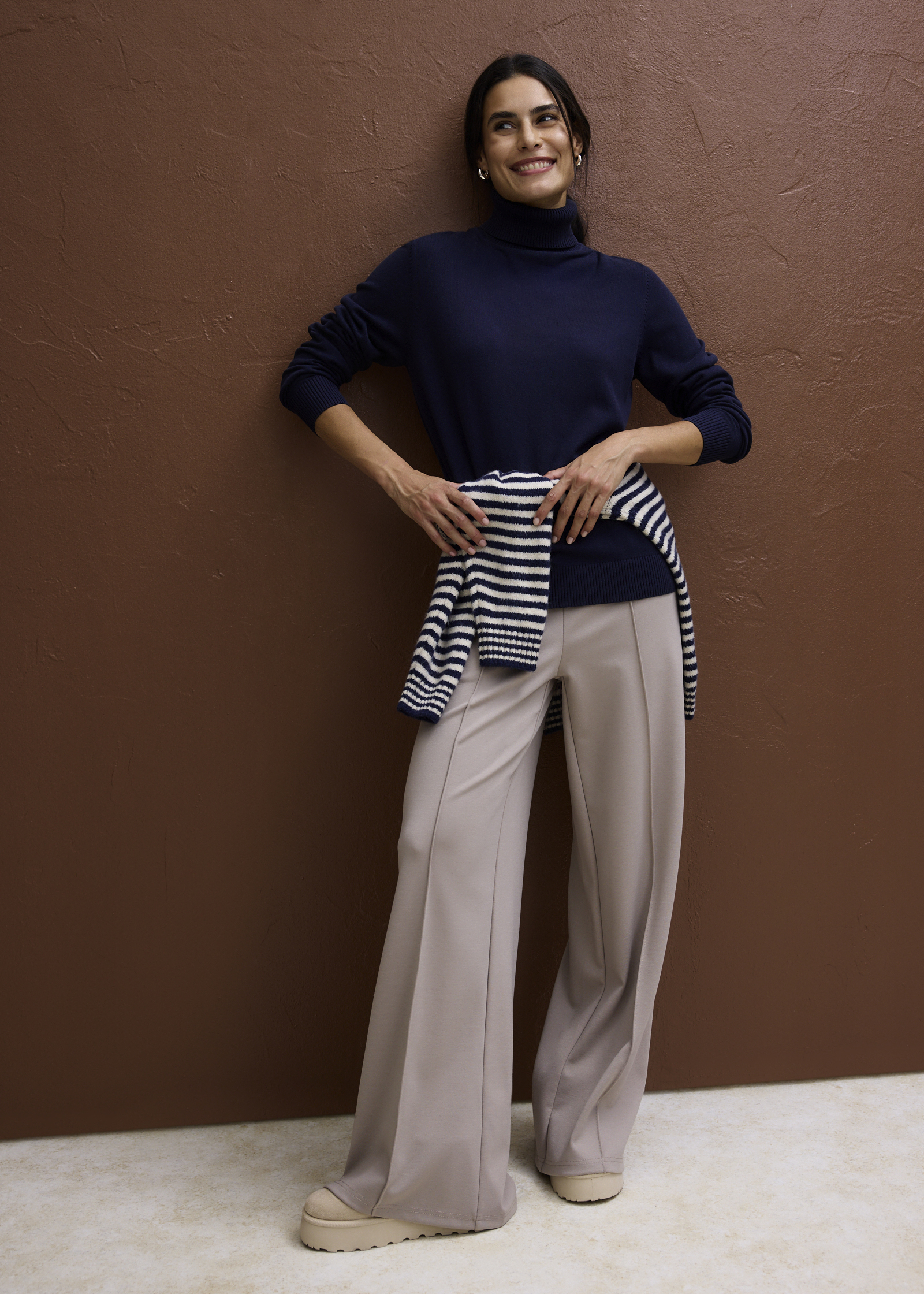 Eleganter dunkelblauer Rollkragenpullover, weite beigefarbene Hose und gestreifter Pullover um die Hüfte.