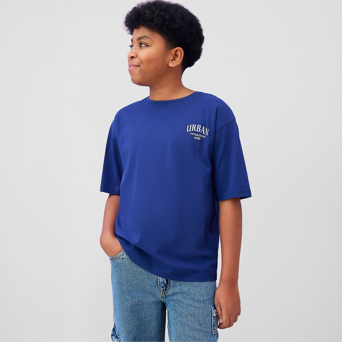 Er trägt ein lässiges blaues T-Shirt mit "Urban" Aufdruck und helle Jeans.