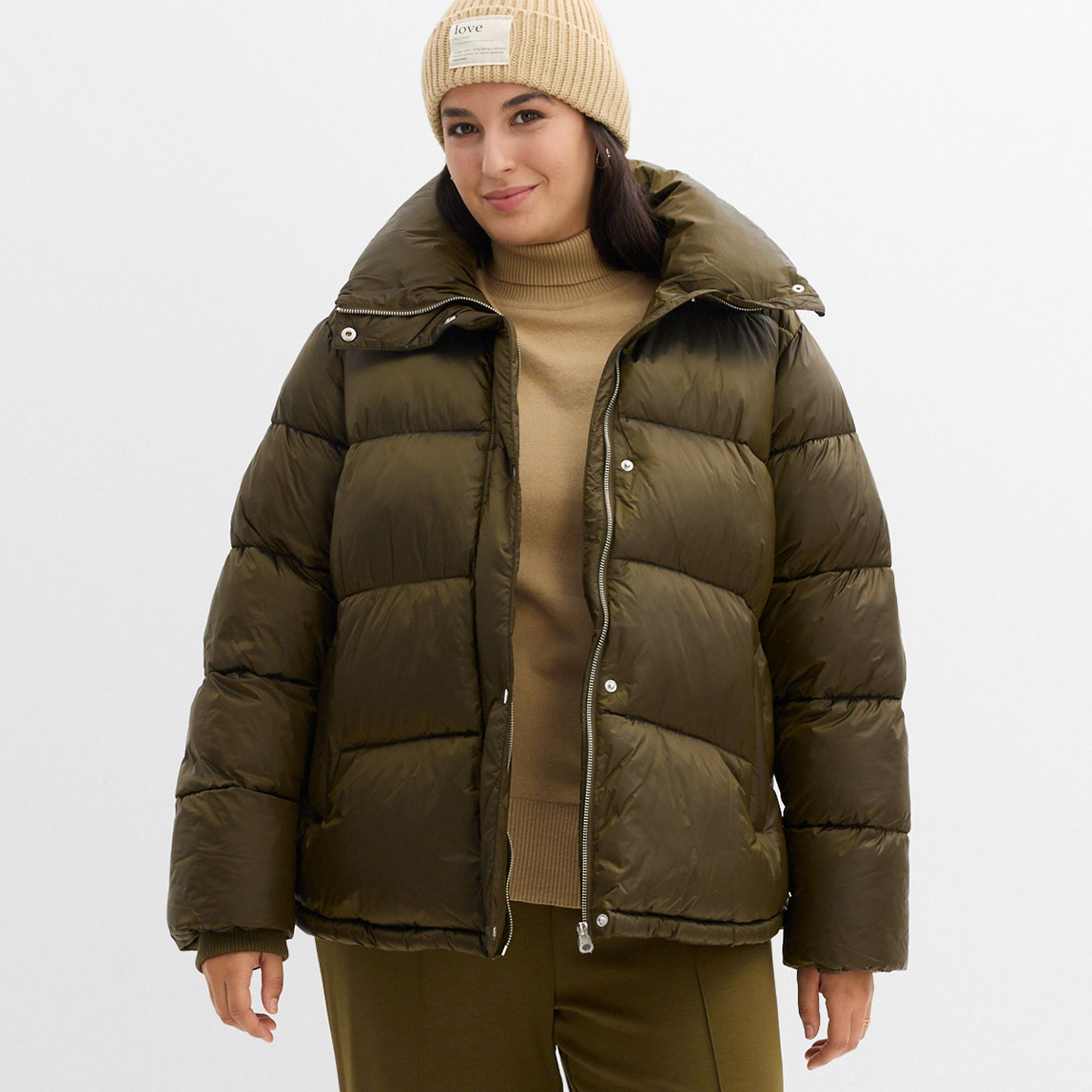 Warme Daunenjacke in Olivgrün, dazu eine beige Mütze und ein heller Pullover.